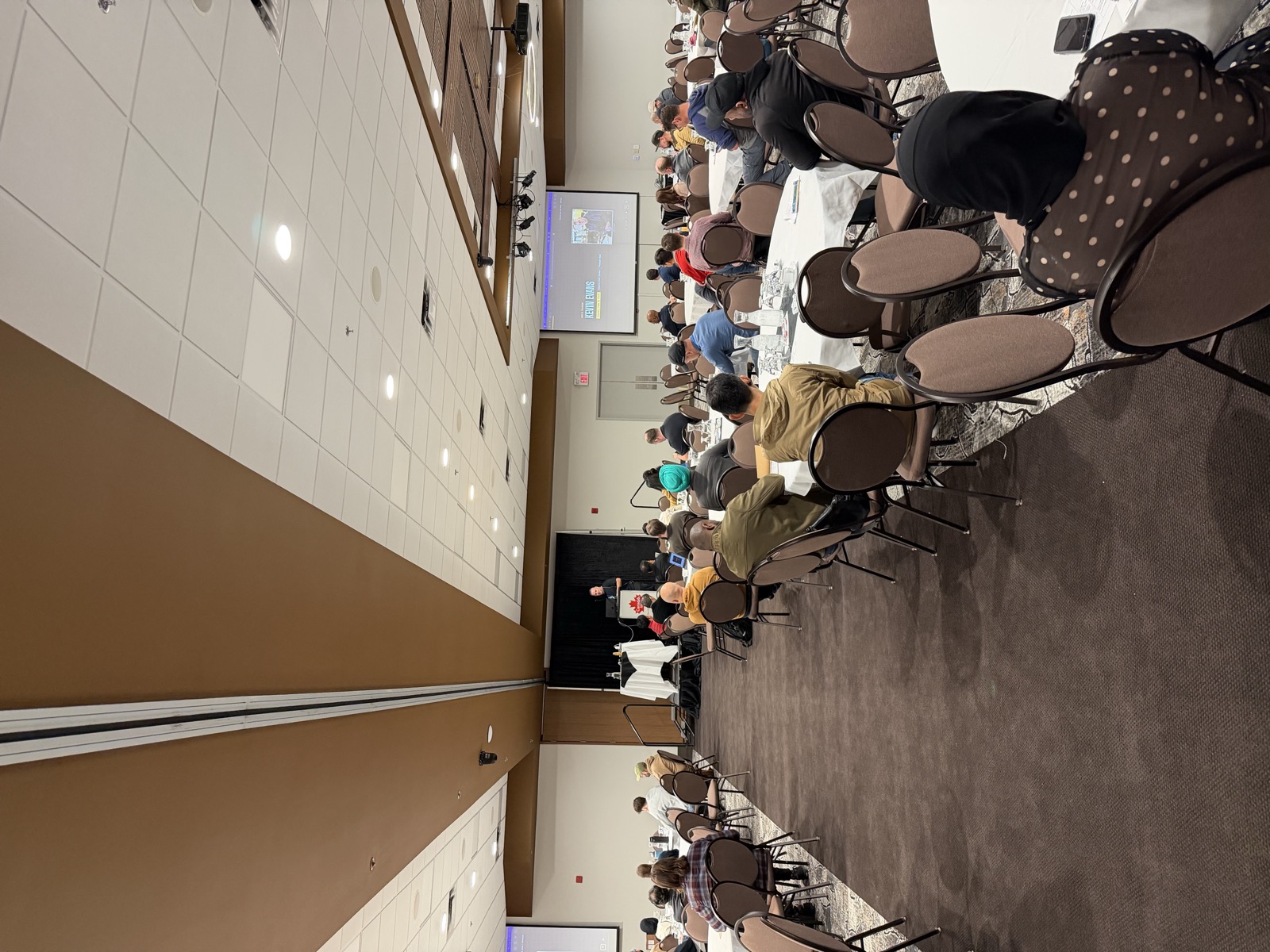 Kevin Evans presenting at a podium at Prairie Dev Con Winnipeg 2026, with a 'Who's Talking: Kevin Evans' introduction slide displayed on screen behind him.