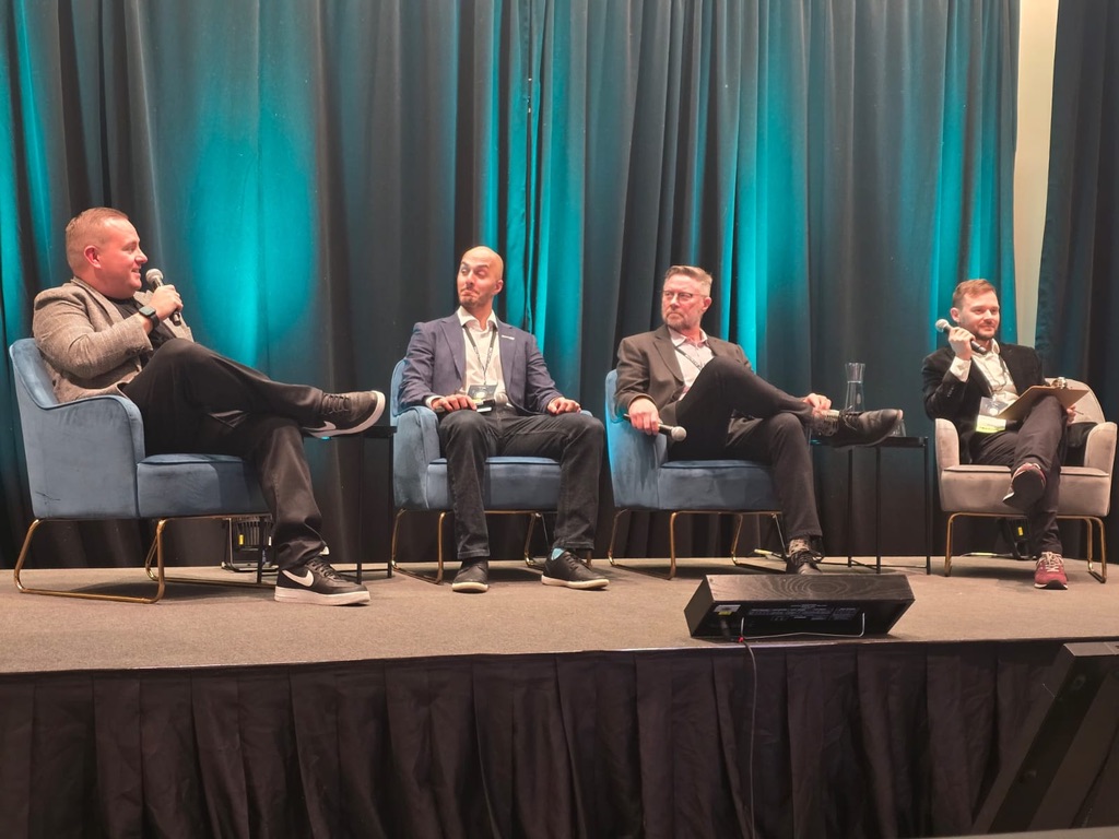 Four panelists seated in armchairs on the YYC DataCon 2026 stage, three holding microphones mid-discussion, in front of a teal curtain backdrop